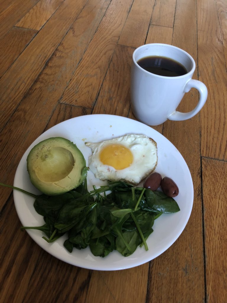 breakfast plate with sunny side up egg, avocado, spinach and white mug with black coffee