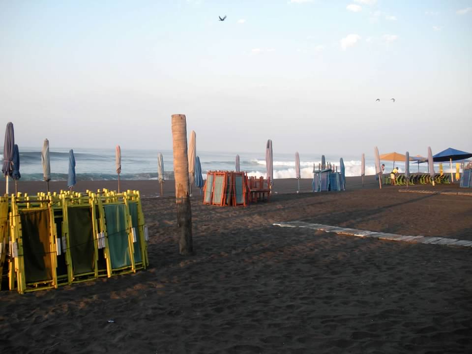 Beach scene with folded chairs and umbrellas, the sand is black 