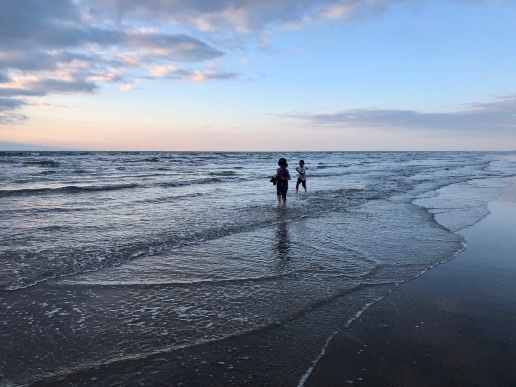 Two kids running in the ocean at sunset on a beach vacation to Port Aransas